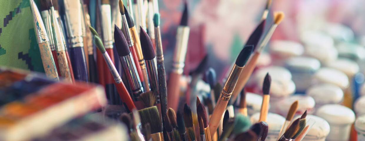 Paint brushes and watercolor paints on the table in a workshop, selective focus, close up.