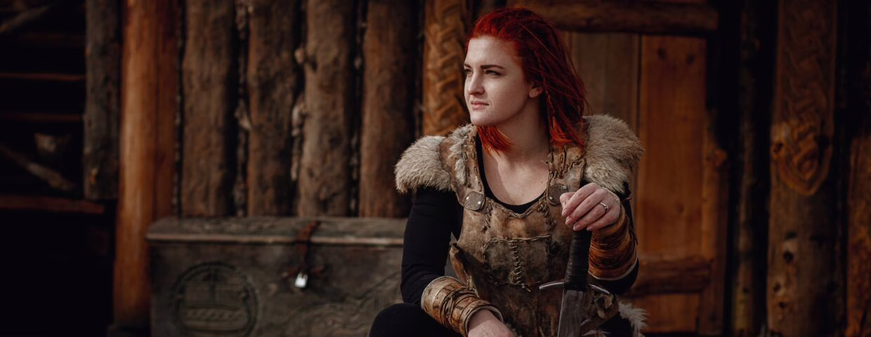 Viking girl with red hair. In the hands of the sword to fight the enemy. Reconstruction of a medieval scene. Against the backdrop of a large viking village.